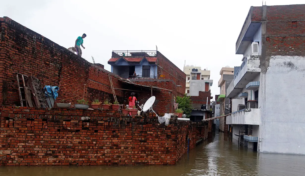 Seorang warga saat terjebak banjir di Allahabad, India (21/8).Selain tiang listrik, warga juga naik ke atap untuk melindungi diri dari arus banjir. (REUTERS/Jitendra Prakash)
