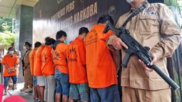 Polisi bersenjata laras panjang berjaga dekat para tersangka kasus narkotika jenis sabu dan  ekstasi diperlihatkan saat konferensi pers di Mabes Polri, Jakarta, Rabu (22/2/2023). Ketujuh tersangka yang diringkus dari dua kasus itu berinisial AA, I, RW, KR, ZA, M, dan RS. (Liputan6.com/Angga Yuniar)