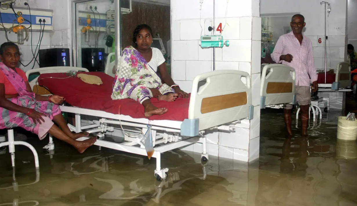Pasien dan anggota keluarganya berada di dalam bangsal yang tergenang banjir di Nalanda Medical College Hospital, daerah Bihar, India, 29 Juli 2018. Rumah sakit itu digenangi air kotor dengan sejumlah ikan terlihat berenang memenuhi lantai. (AFP PHOTO)