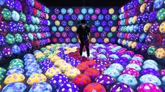Seorang anggota staf berjalan melalui instalasi digital interaktif bernama "Rapidly Rotating Bouncing Sphere Caterpillar House" selama pratinjau media "teamLab Forest" di gedung hiburan BOSS E・ZO FUKUOKA di Fukuoka, Jepang, Jumat (16/7/2021). (YUKI IWAMURA/AFP)
