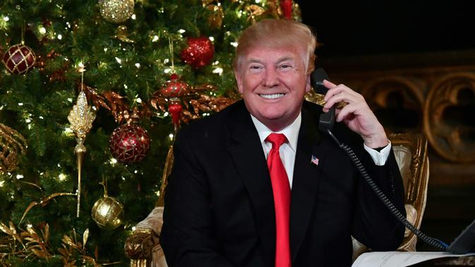 Presiden AS Donald Trump tersenyum saat berbicara di telepon pada malam natal di Palm Beach, AS (24/12). Donald Trump dan istrinya sibuk berbicara di telepon dengan anak-anak saat mengiktui NORAD Tracks Santa. (AFP Photo/Nicholas Kamm)
