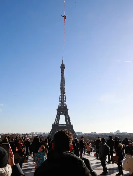 Sejumlah orang melihat aksi menegangkan seniman trapeze, Nathan Paulin berjalan di seutas tali dari Menara Eiffel menuju alun-alun Trocadero, Paris, 9 Desember 2017. Pria 22 tahun itu melakukan penyeberangan sejauh 2.198 kaki. (JACQUES DEMARTHON/AFP)