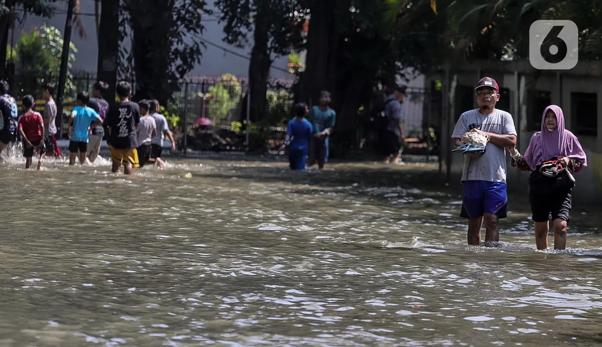 Warga melintasi genangan air yang merendam jalan di kawasan Kampung Makasar, Jakarta Timur, Senin (7/7/2025). (Liputan6.com/Herman Zakharia)