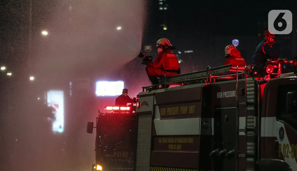 Petugas dari Dinas Penanggulan Kebakaran dan Penyelamatan DKI Jakarta menyemprotkan cairan disinfektan di sekitar Jalan Jenderal Sudirman-MH Thamrin, Jakarta, Kamis (31/12/2020). Jalan ini ditutup pada 31 Desember 2020 pukul 20.00 WIB hingga 1 Januari 2021 pukul 03.00 WIB. (Liputan6.com/Johan Tallo)