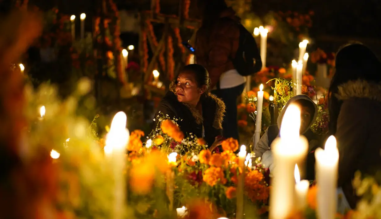 Kerabat menghabiskan malam di samping makam orang tercinta pada perayaan Hari Kematian di pemakaman Arocutin, Michoacan, Meksiko, 1 November 2021. Dalam tradisi ini keluarga menghias makam serta bermalam di kuburan menemani orang tercinta yang telah meninggal. (AP Photo/Eduardo Verdugo)