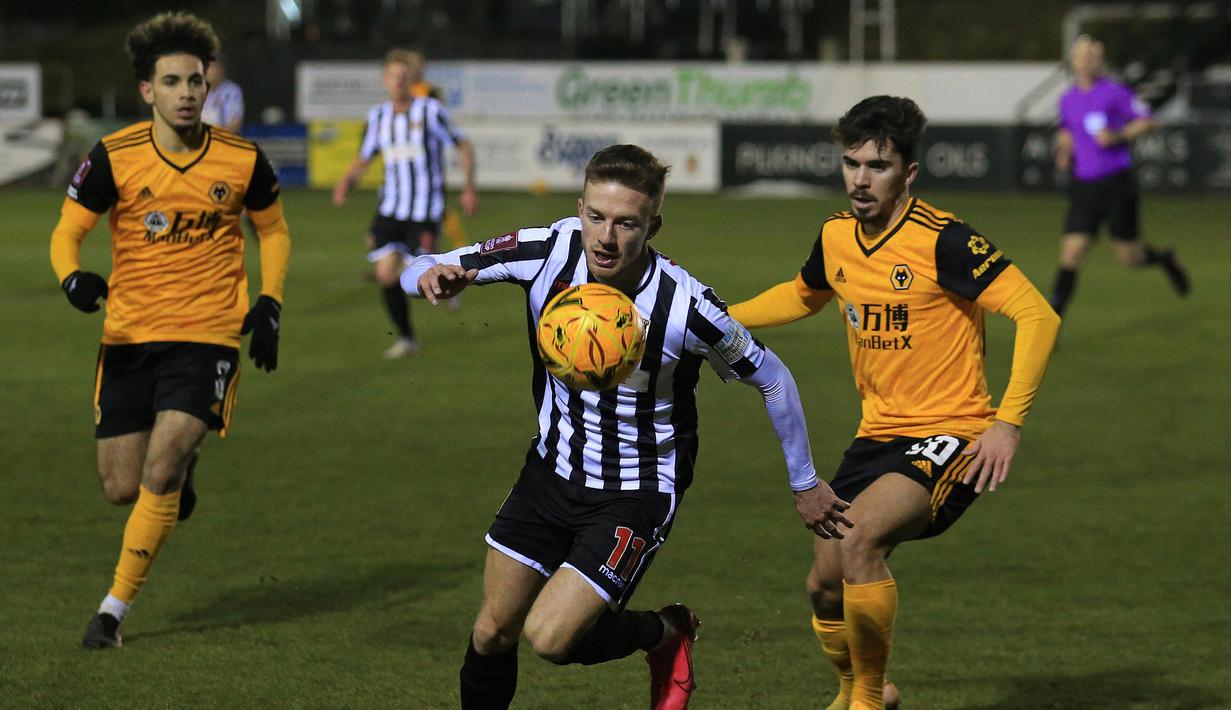 Gelandang Chorley, Elliot Newby (tengah) menguasai bola dibayangi gelandang Wolverhampton Wanderers, Vitinha dalam laga babak keempat Piala FA 2020/21 di Victory Park Stadium, Jumat (22/1/2021). Chorley kalah 0-1 dari Wolverhampton. (AFP/Lindsey Parnaby)