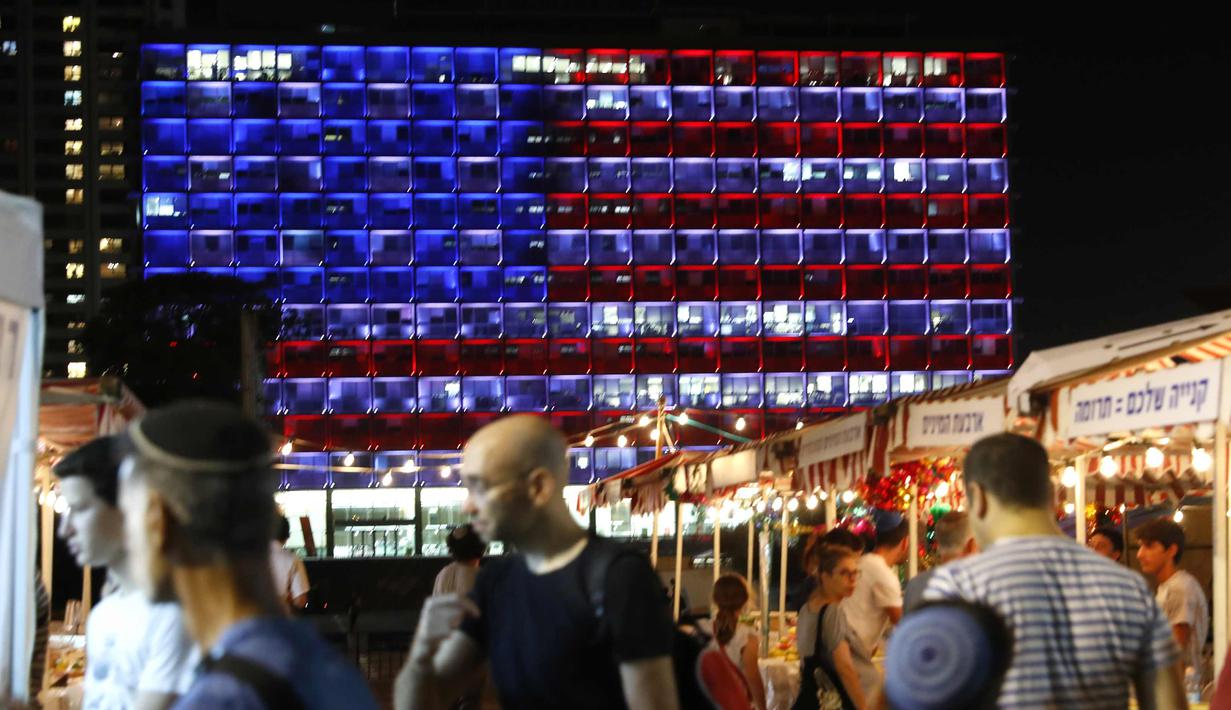 Warga melintas di dekat balai kota Tel Aviv yang dihiasi warna bendera AS untuk menghormati korban penembakan brutal di Las Vegas di Rabin Square, Tel Aviv (2/10). Pelaku penembakan diketahui bernama Stephen Paddock 64 tahun. (AFP Photo/Jack Guez)