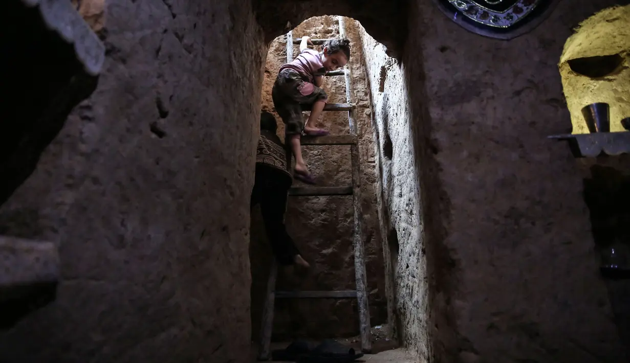 Dua orang bocah menggunakan tangga memasuki ruang bawah tanah Abu Omar di Douma, Damaskus, Suriah, (30/10). Ruang bawah tanah ini memiliki satu kamar tidur dilengkapi ventilasi udara dan penerangan. (AFP PHOTO/Sameer Al-Doumy)