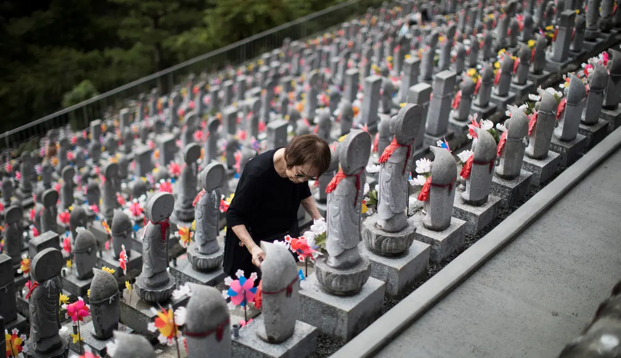 Seorang wanita menyalakan lilin di depan patung Jizo yang didedikasikan untuk jiwa anak-anak yang telah meninggal dunia di Kuil Buddha Jizoji, Oganomachi, Prefektur Saitama, Jepang, Senin (13/8). (Behrouz Mehri/AFP)