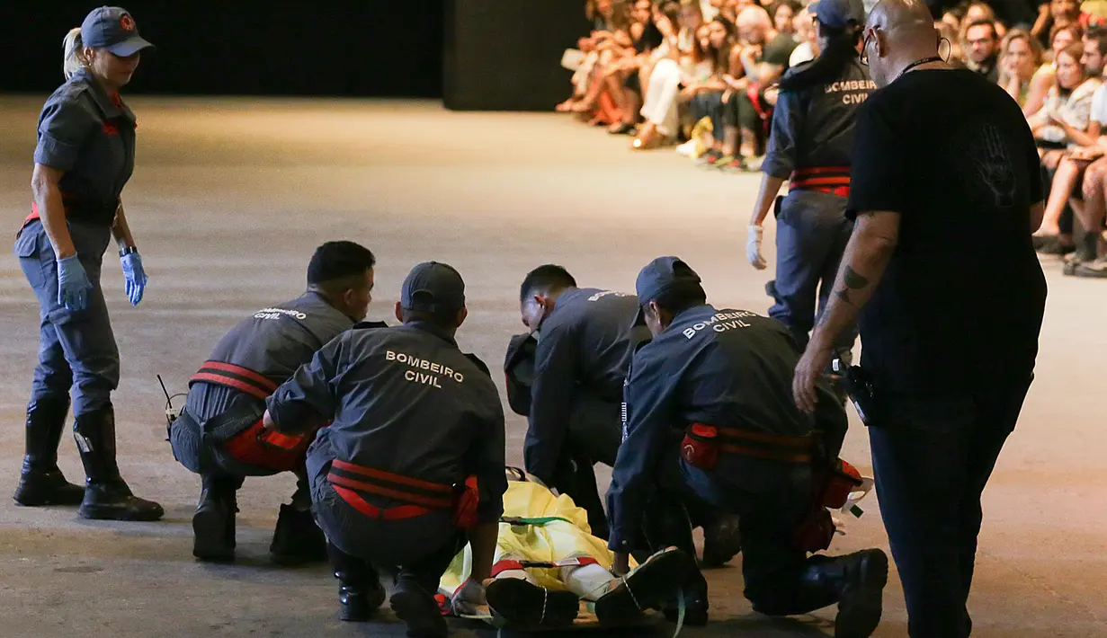 Petugas medis membawa model Tales Cotta saat terjatuh di catwalk Sao Paulo Fashion Week, Sao Paulo, Brasil, 27 April 2019. Di tengah situasi yang mengguncang, semua orang akhirnya memutuskan untuk mempertahankan parade. (Leco Viana Thenews2 via AP)
