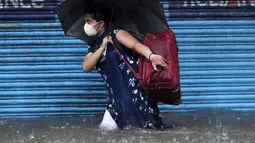 Seorang wanita mengenakan masker sebagai tindakan pencegahan terhadap virus corona melintasi banjir saat hujan lebat di Mumbai, India, Rabu, (5/8/2020). Musim hujan India berlangsung dari Juni hingga September. (AP Photo/Rajanish Kakade)