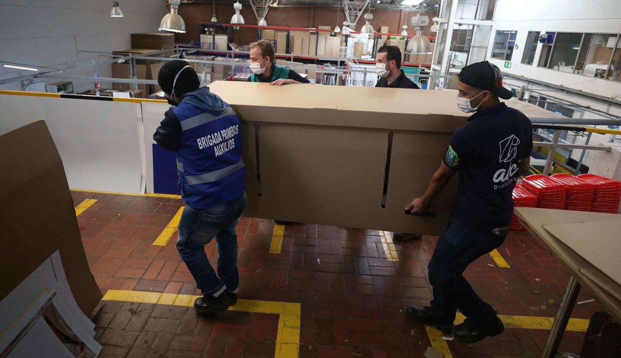 Pekerja perusahaan membawa produk berisi rekan mereka saat mendemonstrasikan desain kardus yang dapat berfungsi sebagai tempat tidur rumah sakit dan peti mati di Bogota, Kolombia, Jumat (8/5/2020). Perusahaan ini menanggapi kekurangan tempat tidur dan peti mati selama pandemi.  (AP/Fernando Vergara)