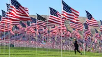 Seorang wanita berjalan melewati pameran bendera AS untuk peringatan 20 tahun serangan 9/11 di Pepperdine University di Malibu, Rabu (8/9/2021). Selama 14 tahun, universitas itu memperingati tragedi 11 September 2001 dengan mengibarkan sekitar 3.000 bendera Amerika. (Frederic J. BROWN/AFP)