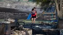 Seorang wanita dan anaknya melewati rumah mereka yang hangus akibat kebakaran hutan di Ashcroft First Nation, British Columbia, Kanada, (9/7). Musibah ini mengakibatkan terganggunya operasi kayu dan pertambangan. (Darryl Dyck/The Canadian Press via AP)