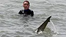 Seekor hiu berenang melewati perempuan dengan pakaian selam di Laut Mediterania di lepas pantai kota Hadera di utara Tel Aviv, Israel, Selasa (20/4/2021). Fenomena yang menjadi perhatian warga ini diduga akibat suhu air laut Mediterania berubah menjadi hangat. (JACK GUEZ/AFP)