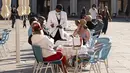 Pramusaji mengobrol dengan turis yang duduk di teras kafe Piazza San Marco di Venesia pada 20 Mei 2021. Turis kembali berdatangan menikmati keindahan Venesia, yang sering dijuluki kota paling romantis di dunia, setelah Italia menghapus kewajiban karantina bagi pendatang. (Marco Bertorello/AFP)