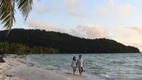 Turis berjalan di sepanjang pantai di pulau Phu Quoc selatan Vietnam (19/11/2021). Vietnam membuka kembali pulau resor Phu Quoc bagi pengunjung asing yang telah divaksinasi. (AFP/Nhac Nguyen)