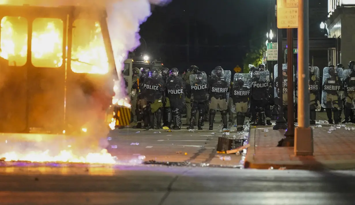Polisi berdiri dekat truk sampah yang terbakar saat protes di Kenosha, Wisconsin, Amerika Serikat, Senin (24/8/2020). Protes dipicu oleh penembakan Jacob Blake oleh petugas polisi Kenosha sehari sebelumnya. (AP Photo/Morry Gash)