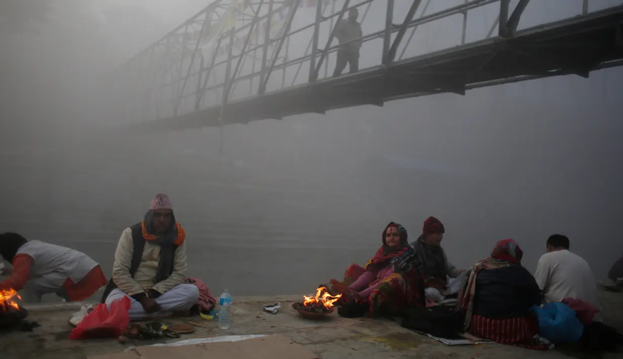 Sejumlah warga Nepal duduk di dekat api dengan diselimuti kabut saat mengikuti festival Gaya Aunsi di Kathmandu, Nepal (21/12). (AP Photo/Niranjan Shrestha)
