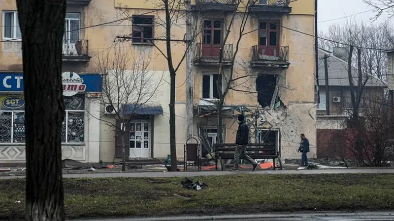 Seorang pria berjalan melewati sebuah gedung apartemen pada 2 Maret yang dirusak oleh penembakan Rusia di Mariupol, Ukraina. (Evgeniy Maloletka/AP)