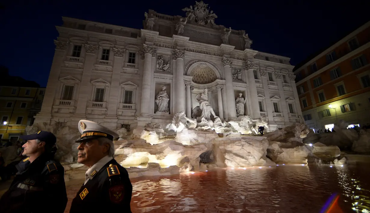 Polisi setempat berdiri dekat air mancur Trevi di Roma, Italia yang berubah warna jadi merah, 26 Oktober 2017. Peristiwa tersebut terjadi setelah seorang pria membuang pewarna ke dalam kolam air mancur sebagai bentuk protes. (Filippo MONTEFORTE/AFP)