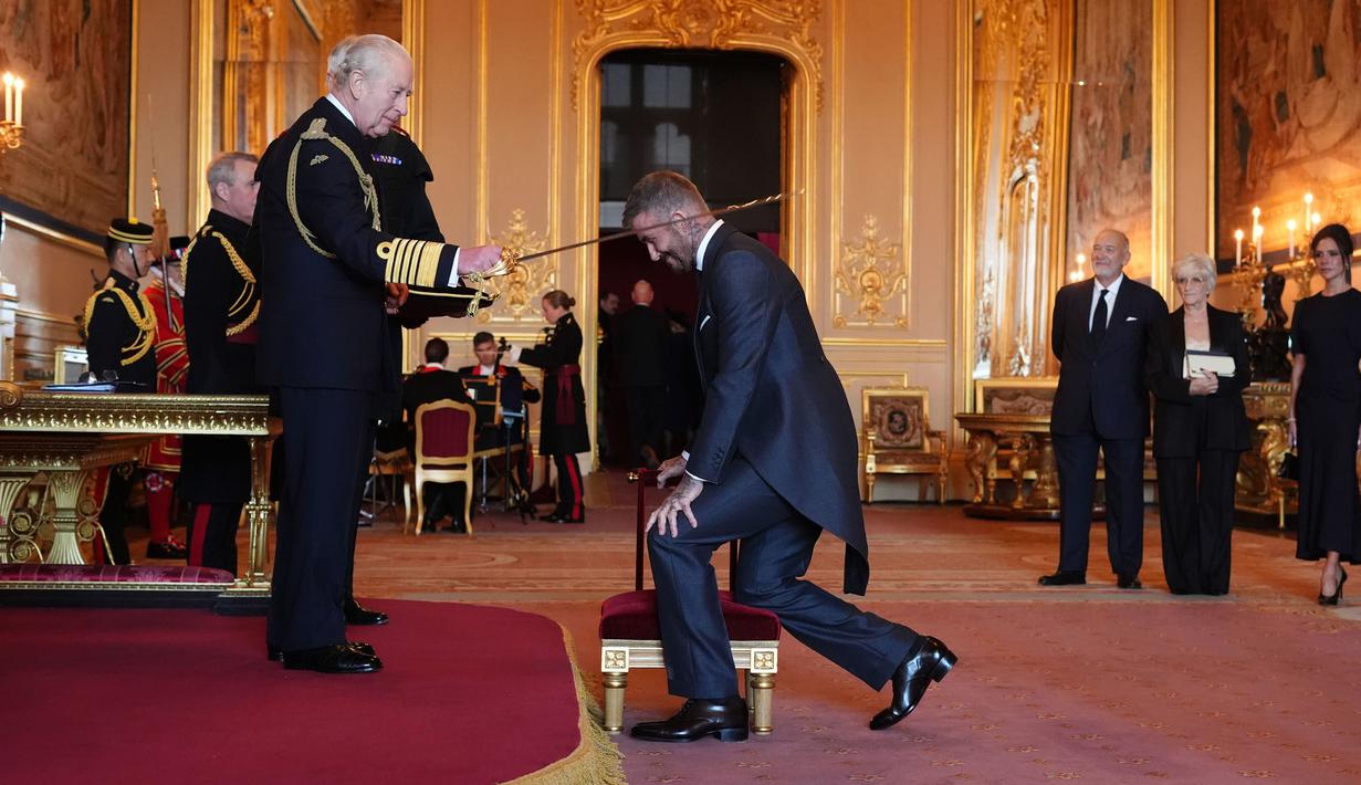 Mantan pesepak bola, David Beckham (kanan) dianugerahi gelar Ksatria oleh Raja Inggris, Charles III dalam upacara penobatan di Kastil Windsor, Berkshire, Inggris, Selasa (04/11/2025) waktu setempat. (AP Photo/PA/Jonathan Brady)