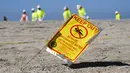 Sebuah tanda peringatan ditampilkan saat pekerja dengan pakaian pelindung membersihkan pantai yang terkontaminasi tumpahan minyak di Huntington Beach, California, Amerika Serikat, Selasa (5/10/2021). Kebocoran pipa menyebabkan tumpahan minyak di lepas pantai California. (AP Photo/Ringo H.W. Chiu)