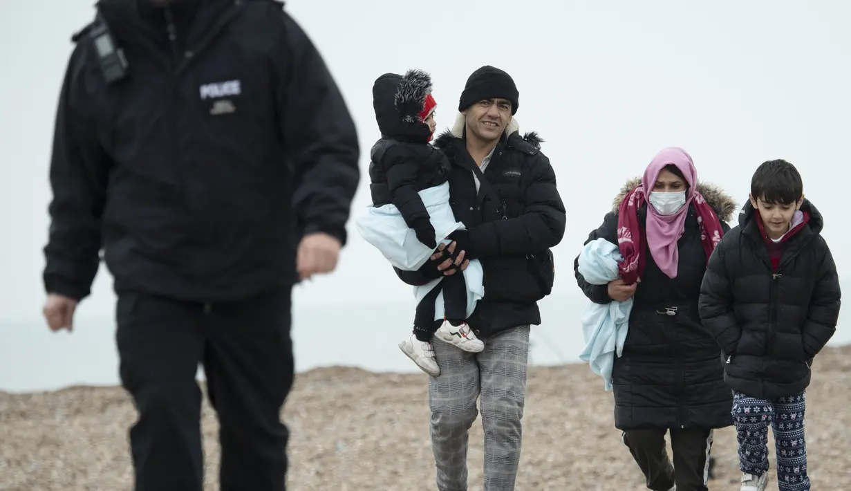 Para migran berjalan di sepanjang pantai setelah dibantu ke darat dari sekoci RNLI (Royal National Lifeboat Institution) menyusul penyelamatan mereka saat melintasi Selat Inggris di Dungeness, Inggris tenggara (24/11/2021). (AFP/Ben Stansall)