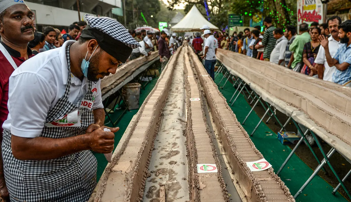 Seorang tukang roti menyelesaikan kue sepanjang 6,5 km untuk kue terpanjang dunia, di Thrissur di negara bagian Kerala, India selatan (15/1/2020). Ratusan pembuat roti dan koki di India selatan membuat kue terpanjang di dunia. (AFP/Arun Sankar)