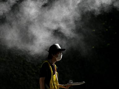 Seorang relawan berjalan di bawah alat penyemprot desinfektan di Tokyo pada 21 Juli 2021 menjelang Olimpiade Tokyo 2020. (AFP/Mohd Rasfan)