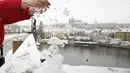 Seorang wanita menaburkan es ke manusia salju di Jembatan Charles abad pertengahan setelah hujan salju pertama di Praha, Republik Ceko (3/12/2020). (AP Photo / Petr David Josek)