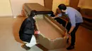 Alejandro Blanchard dan Elio Angulo menempatkan peti mati karton ke dalam peti di kamar mayat di negara bagian Carabobo, Venezuela, Kamis (25/08). Peti mati bernilai ekonomis dibuat dari kertas daur ulang yang ramah lingkungan. (REUTERS/Marco Bello)