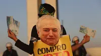 Seorang wanita memegang uang palsu dan poster bergambar Presiden Brasil Michel Temer pada unjuk rasa di depan Kongres Nasional, Brasilia, Rabu (2/8). Para demonstran membanjiri jalanan kota sejak Rabu waktu setempat. (AP/Eraldo Peres)