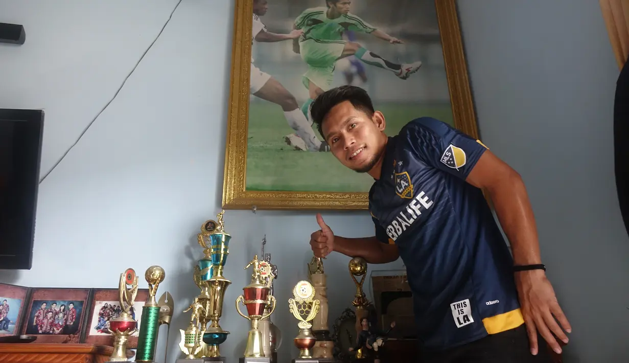 Andik Vermansah berfoto di depan piala yang pernah diraihnya. Selain berlibur ke Lombok, Andik juga mengadakan syukuran sukses meraih gelar juara Piala Malaysia bersama Selangor FA. (Bola.com/Zaidan Nazarul)