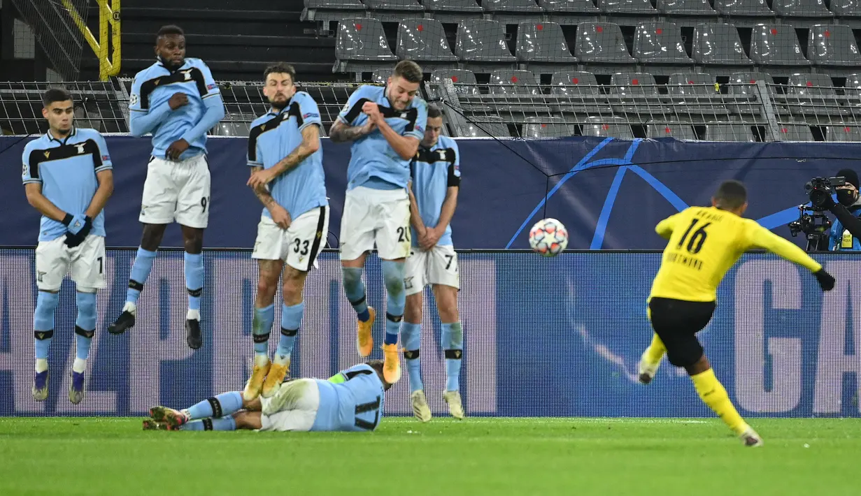 Striker Lazio, Ciro Immobile berbaring di belakang rekan-rekannya yang membuat pagar hidup untuk menjaga tendangan bebas yang dilakukan bek Borussia Dortmund, Manuel Akanji dalam laga lanjutan Liga Champions 2020/21 di Signal Iduna Park, Selasa (1/12/2020). (AFP/Ina Fassbender)