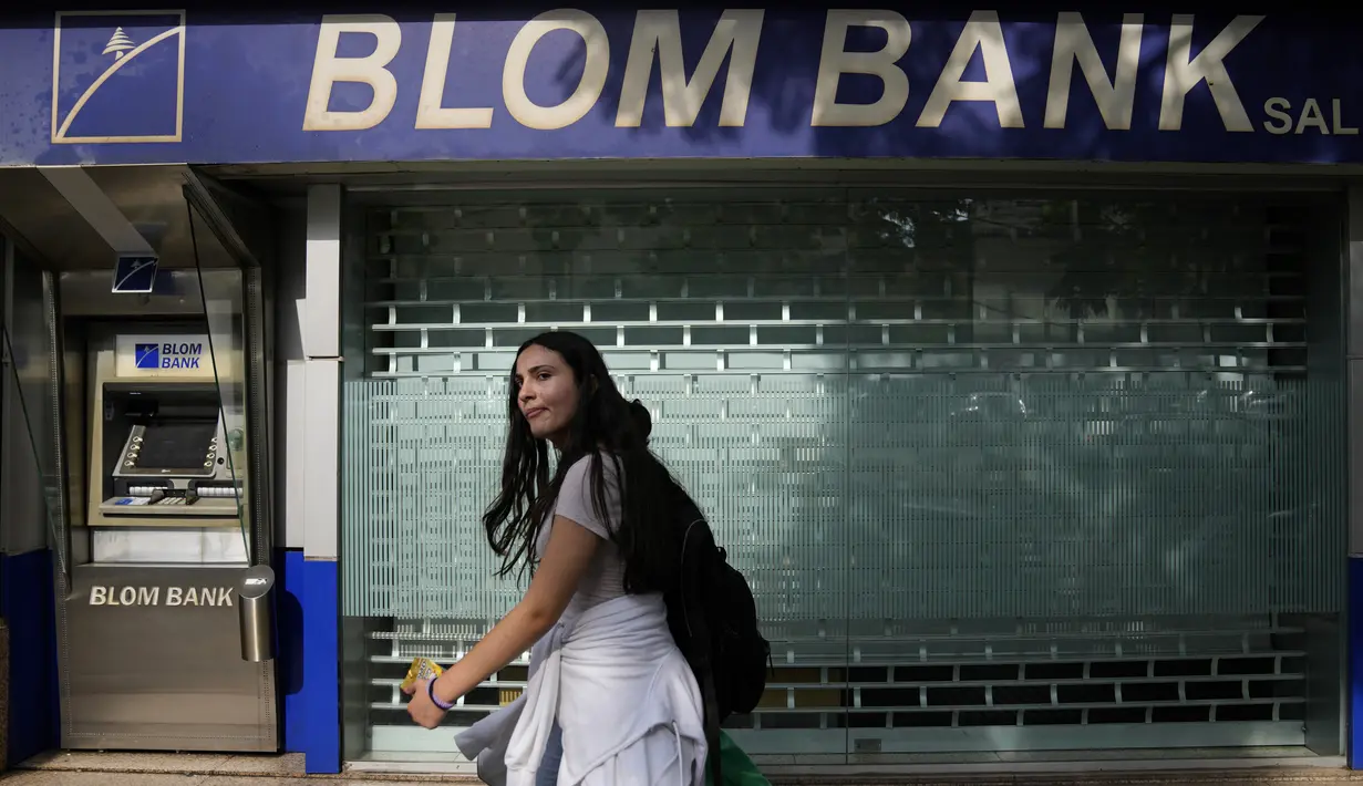 Seorang perempuan melintas di sebuah cabang Bank BLOM yang tutup di Beirut, Lebanon, Selasa (20/9/2022). Ketika cabang bank dibuka kembali, sejumlah bank merencanakan langkah-langkah perlindungan diri yang ketat. Dimana, seluruh nasabah diperiksa dan hanya menerima mereka yang memiliki janji temu terjadwal. (AP Photo/Hassan Ammar)