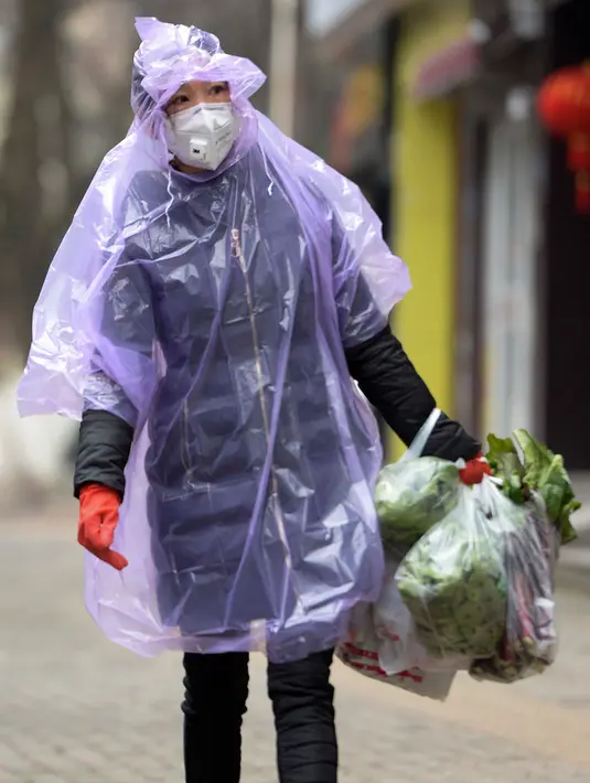 Seorang perempuan bermasker mengenakan jas hujan membawa bahan makanan untuk melindungi diri dari wabah virus corona di Wuhan, China, 10 Februari 2020. Awal tahun 2020 ini, masyarakat dunia dikejutkan dengan hadirnya virus corona COVID-19 yang mematikan asal Wuhan, China. (Chinatopix via AP)