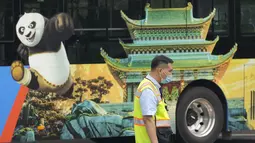 Petugas lalu lintas berdiri di dekat bus dengan iklan untuk taman hiburan Universal Studios selama uji coba di Beijing (31/8/2021). Perusahaan menetapkan tanggal pembukaan 20 September, menurut pernyataan dan video yang diposting di situs media sosial China WeChat. (AP Photo/Ng Han Guan)