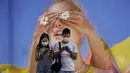Pasangan yang memakai masker melihat ponsel mereka di depan poster besar di Hong Kong pada 27 Juli 2020. (AP Photo / Vincent Yu)