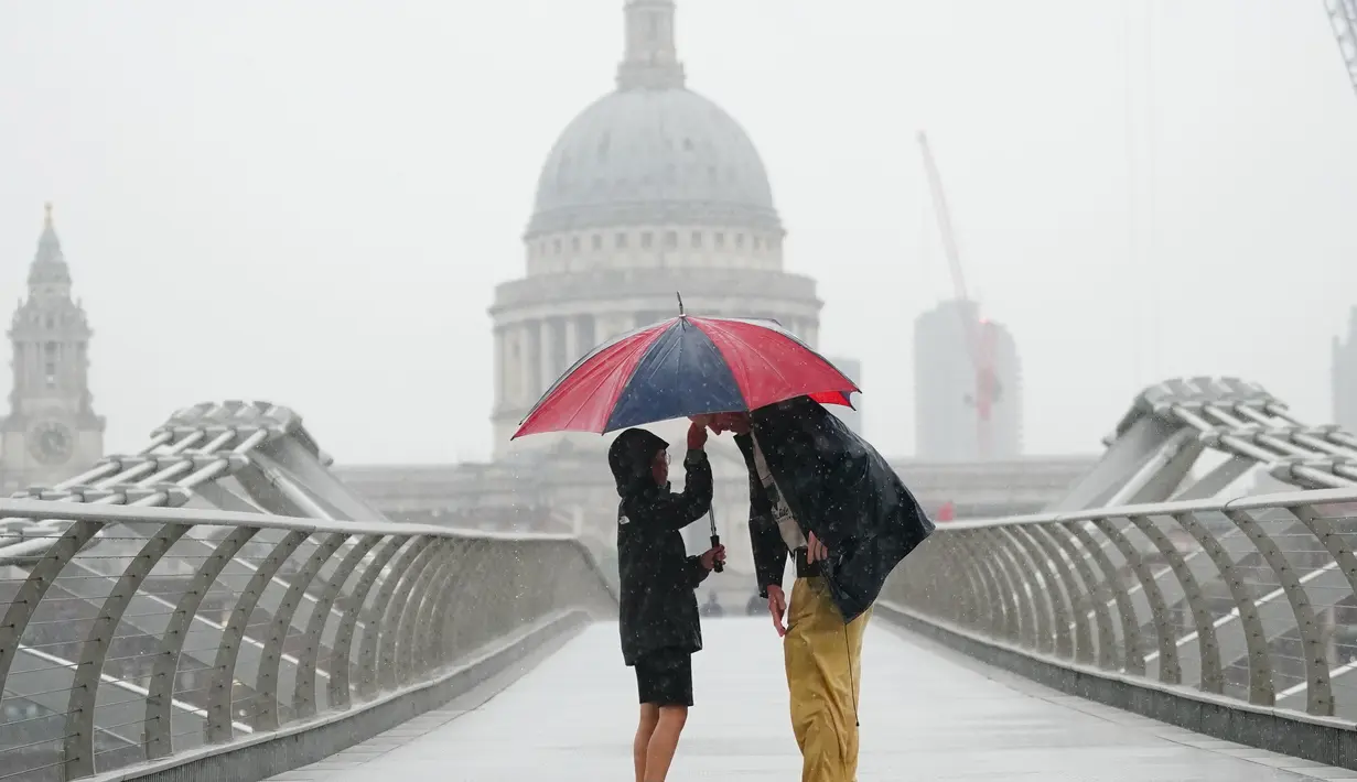 Orang-orang berlindung dengan payung di tengah hujan di London, Rabu (17/8/2022). Setelah berminggu-minggu cuaca terik, yang telah menyebabkan kekeringan dan membuat tanah kering, peringatan badai petir kuning dari Kantor Meteorologi memperkirakan hujan lebat dan badai petir yang bisa melanda bagian Inggris dan Wales. (Victoria Jones/PA via AP)