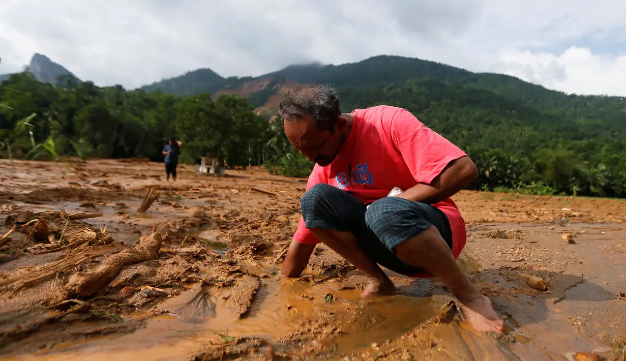 Seorang pria mencoba untuk menemukan sandalnya yang tertimbun lumpur setelah longsor di Desa Elangipitiya, Aranayaka, Sri Lanka (19/5). Ratusan warga dikabarkan hilang akibat tanah longsor tersebut. (REUTERS/Dinuka Liyanawatte)