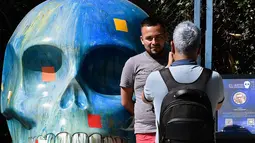 Seorang pria berpose dengan tengkorak yang dihias selama pameran edisi keempat "Mexicraneos" (Mexisculls) di Reforma Avenue, Mexico City pada 23 Oktober 2020. Instalasi sebanyak 55 tengkorak berbagai warna tersebut menghiasi jalanan sebagai bagian dari perayaan Day of the Dead (ALFREDO ESTRELLA/AFP)