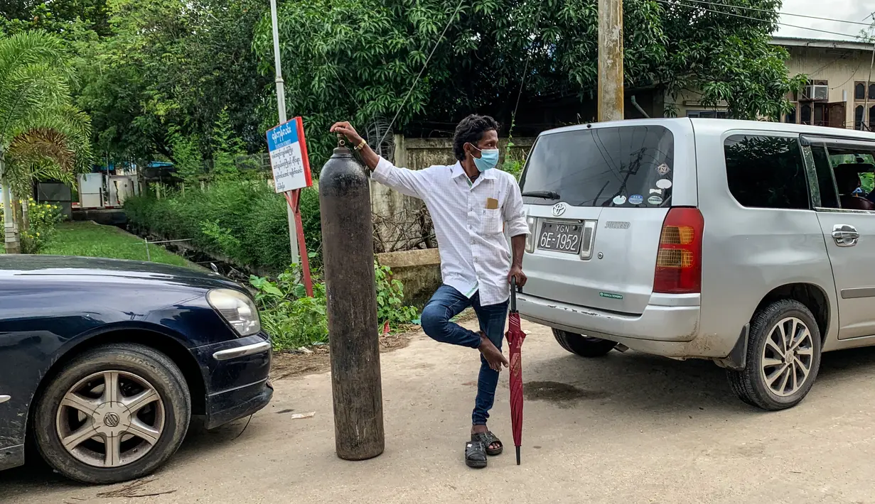 Seorang pria berdiri dengan tabung oksigen saat menunggu untuk mengisi ulangnya di luar sebuah pabrik di Yangon, Myanmar, Minggu (11/7/2021). Para pejabat mengatakan Myanmar mengalami lonjakan kasus COVID-19, memicu kelangkaan pasokan oksigen yang sangat dibutuhkan pasien. (Ye Aung THU/AFP)