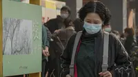 Seorang wanita berjalan melewati poster ketika warga antre menerima suntikan booster di tempat vaksinasi di Beijing, Senin (25/10/2021). Sebuah provinsi di China barat laut yang bergantung pada pariwisata menutup semua lokasi wisata pada Senin usai menemukan kasus baru COVID-19. (AP Photo/Andy Wong)