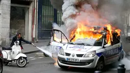 Petugas berusaha memadamkan mobil polisi yang terbakar akibat demo di Paris, Prancis (18/5). Demo buruh tersebut menentang kekerasan polisi dan melawan reformasi hukum yang berakhir bentrok dengan polisi. (REUTERS / Charles Platiau)