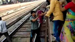 Gambar dari video pada 20 November 2018, seorang pria India menggendong bayi dan memberikan kepada ibunya  setelah terjatuh di samping rel di stasiun kereta api di Mathura, Uttar Pradesh. Bayi satu tahun itu selamat tanpa luka sedikitpun. (NNIS / AFP)
