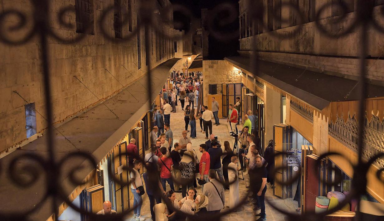 Gambar ini diambil di belakang kisi-kisi balkon pada 29 Agustus 2021 menunjukkan orang-orang berjalan-jalan di "Souq Khan al-Harir" (pasar tertutup sutra) yang dibuka kembali di kota utara Aleppo Suriah setelah upaya rekonstruksi setelah konflik bertahun-tahun. (AFP Photo)