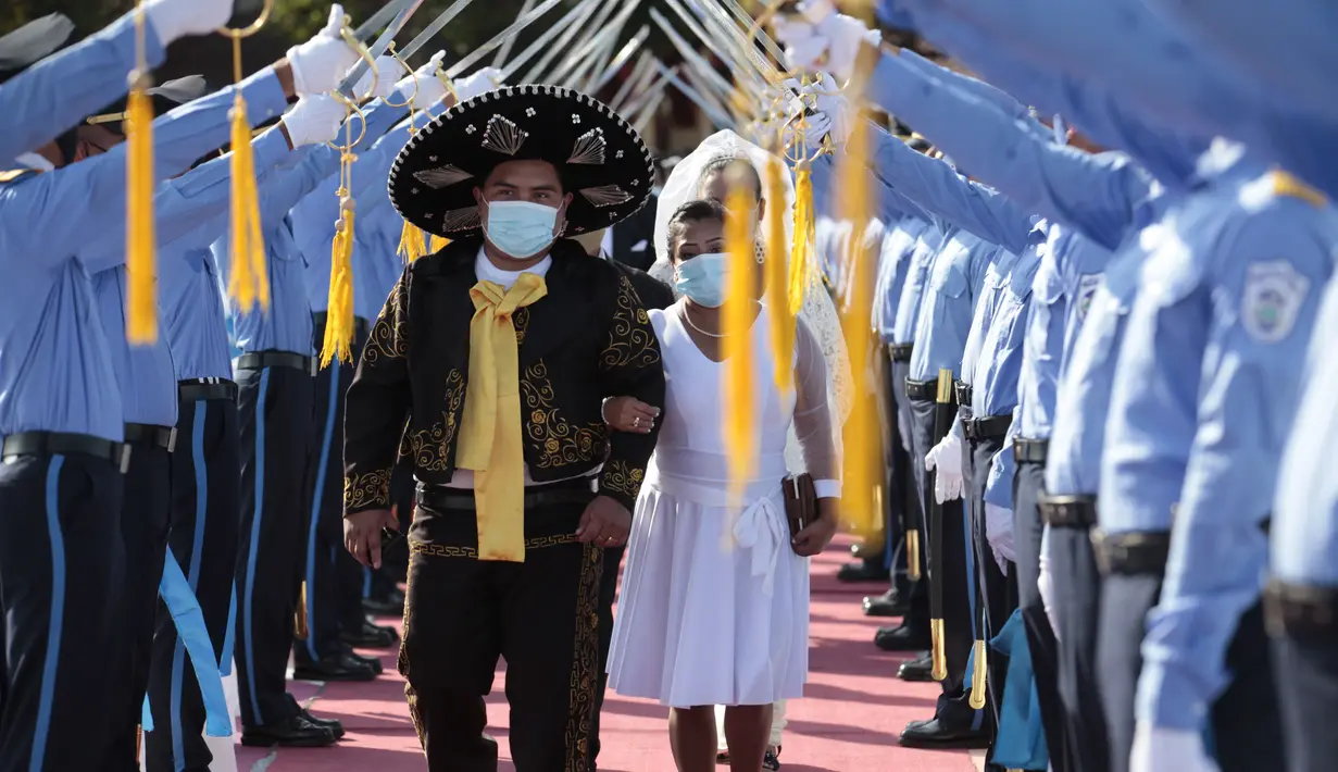 Sepasang suami istri berjalan di bawah lorong pedang kadet polisi saat pernikahan massal di Managua, Nikaragua, Minggu (14/2/2021). Sekitar 400 pasangan mengatakan "I do" pada Hari Valentine pada acara nikah massal gratis. (AP Photo/Diana Ulloa)