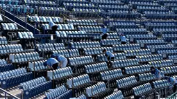 Relawan mendisinfektan kursi setelah pertandingan perebutan medali perunggu softball Olimpiade Tokyo 2020 antara Meksiko dan Kanada di Stadion Baseball Yokohama, pada 27 Juli 2021. Olimpiade yang digelar saat pandemi COVID-19 tersebut menerapkan protokol kesehatan ketat. (KAZUHIRO FUJIHARA / AFP)