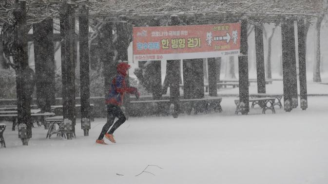 Seorang pelari yang mengenakan masker wajah berlari di salju dekat spanduk yang menunjukkan instruksi jarak sosial sebagai tindakan pencegahan terhadap virus corona di Goyang, Korea Selatan, Kamis (28/1/2021). (AP/Lee Jin-man)